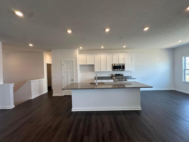 kitchen featuring a kitchen island with sink, appliances with stainless steel finishes, white cabinetry, a sink, and dark wood-style floors