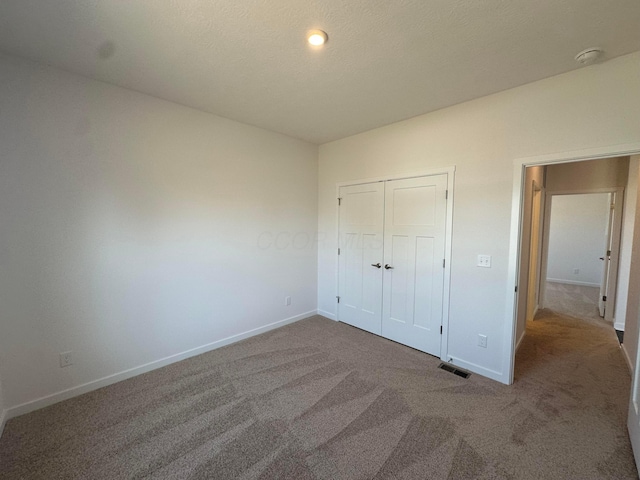 unfurnished bedroom featuring a closet, carpet flooring, a textured ceiling, baseboards, and visible vents