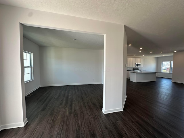 empty room featuring baseboards, a textured ceiling, and dark wood-style flooring