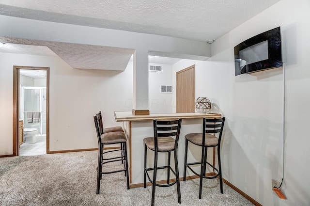 kitchen featuring light colored carpet, a textured ceiling, and a kitchen bar