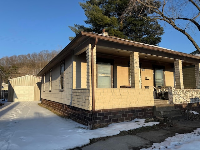 snow covered property featuring a garage, an outbuilding, and covered porch