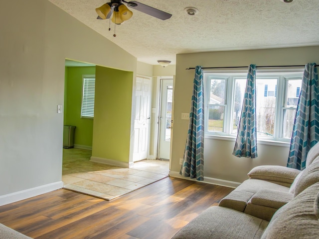 living room with ceiling fan, vaulted ceiling, a textured ceiling, wood finished floors, and baseboards