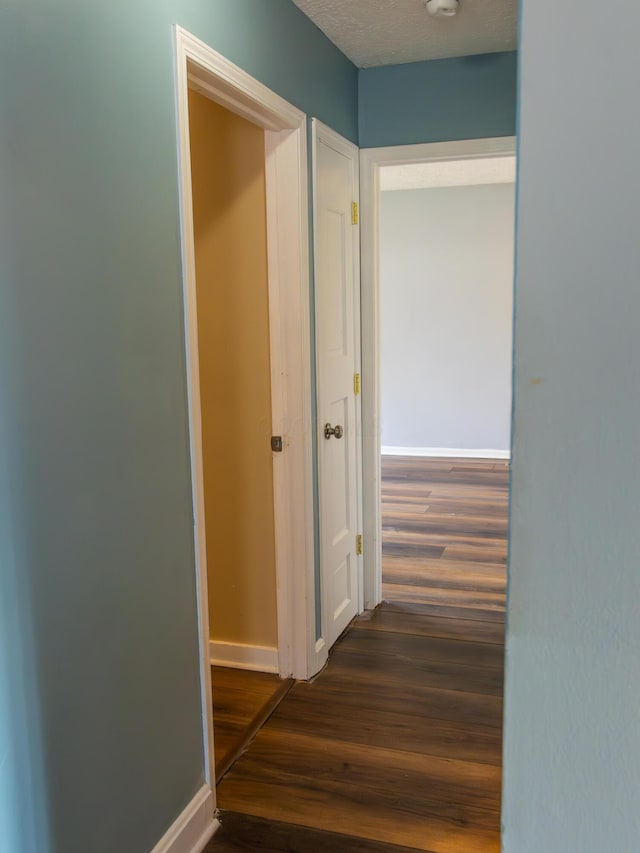 corridor with a textured ceiling, baseboards, and dark wood-style flooring