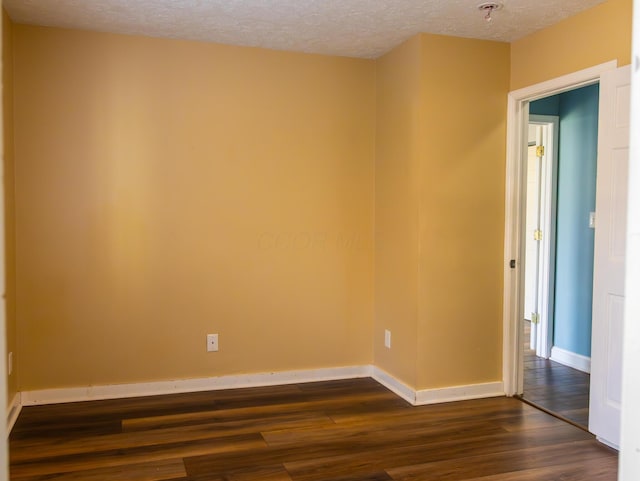 empty room with dark wood finished floors, a textured ceiling, and baseboards