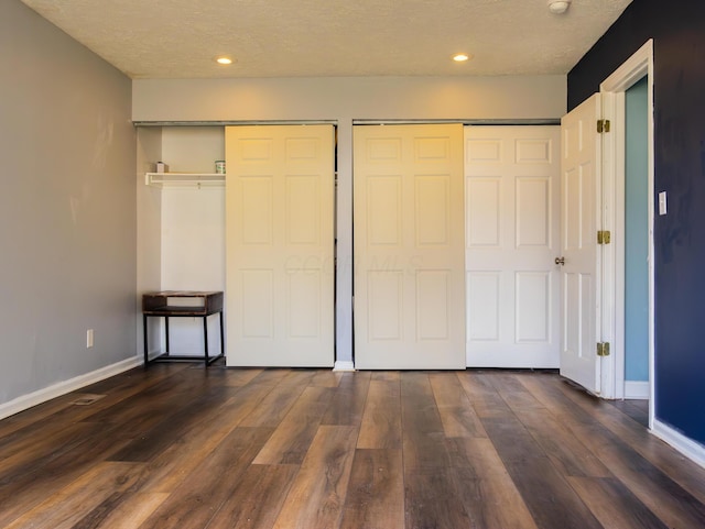 unfurnished bedroom featuring baseboards, dark wood-type flooring, a textured ceiling, two closets, and recessed lighting