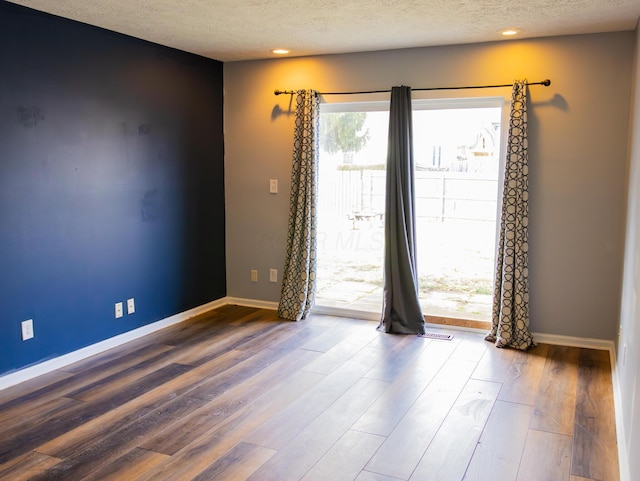 spare room featuring a textured ceiling, wood finished floors, and baseboards