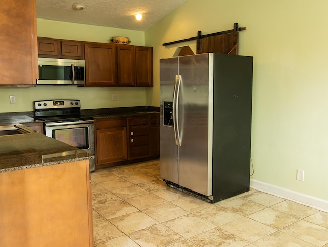 kitchen featuring stainless steel appliances, lofted ceiling, a barn door, a textured ceiling, and baseboards