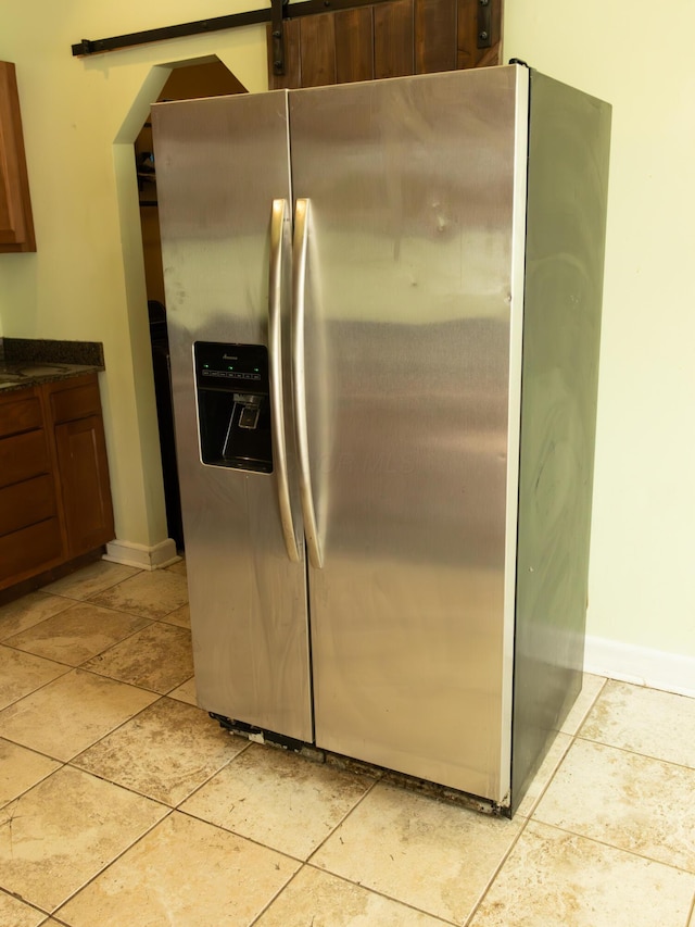 kitchen featuring dark countertops, stainless steel refrigerator with ice dispenser, baseboards, and light tile patterned floors