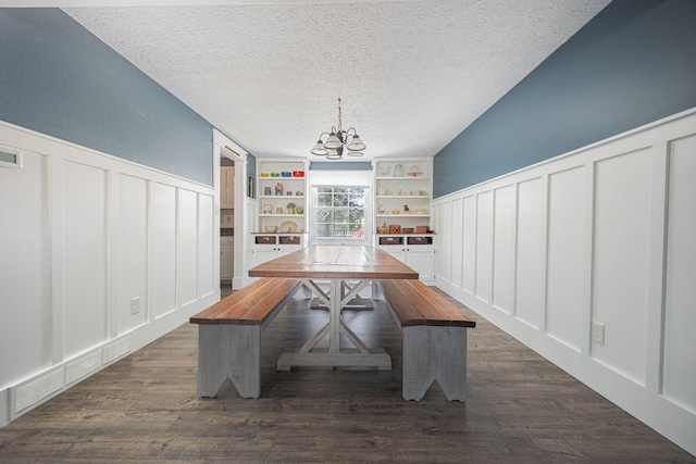 unfurnished dining area featuring dark wood-type flooring, a notable chandelier, a textured ceiling, and built in shelves