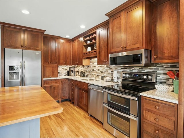 kitchen with appliances with stainless steel finishes, sink, light stone counters, and light wood-type flooring