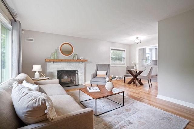 living room with sink, a stone fireplace, light wood-type flooring, and a wealth of natural light