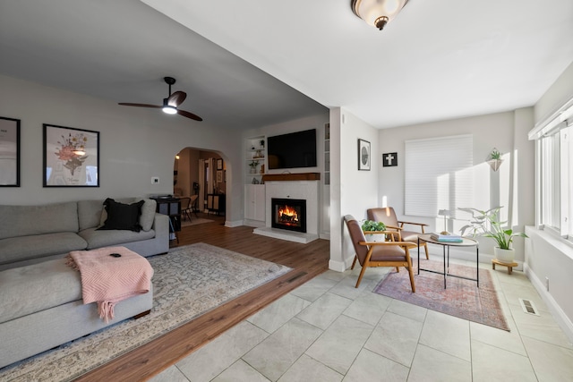 living room with ceiling fan, a fireplace, and built in features