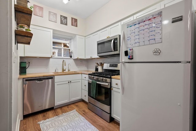 kitchen with sink, butcher block countertops, white cabinetry, tasteful backsplash, and stainless steel appliances