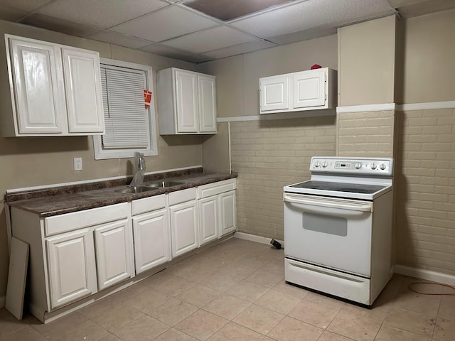 kitchen with sink, a paneled ceiling, white range with electric cooktop, white cabinetry, and brick wall