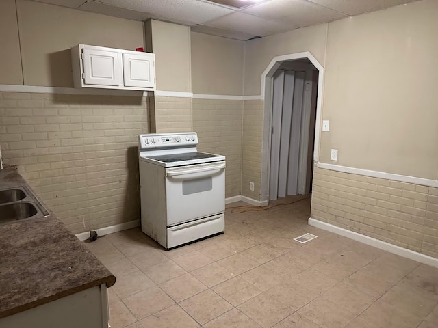 kitchen with sink, white cabinets, white range with electric cooktop, brick wall, and a drop ceiling