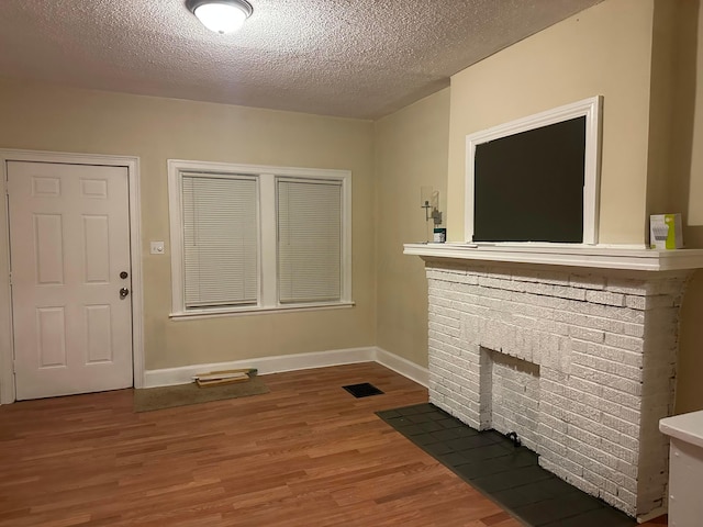 unfurnished living room featuring hardwood / wood-style flooring, a brick fireplace, and a textured ceiling