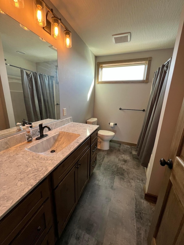 full bath featuring visible vents, toilet, a textured ceiling, vanity, and baseboards