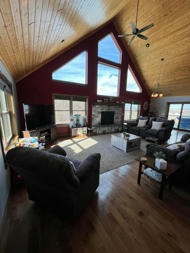 living room with ceiling fan with notable chandelier, high vaulted ceiling, wood-type flooring, a stone fireplace, and wooden ceiling