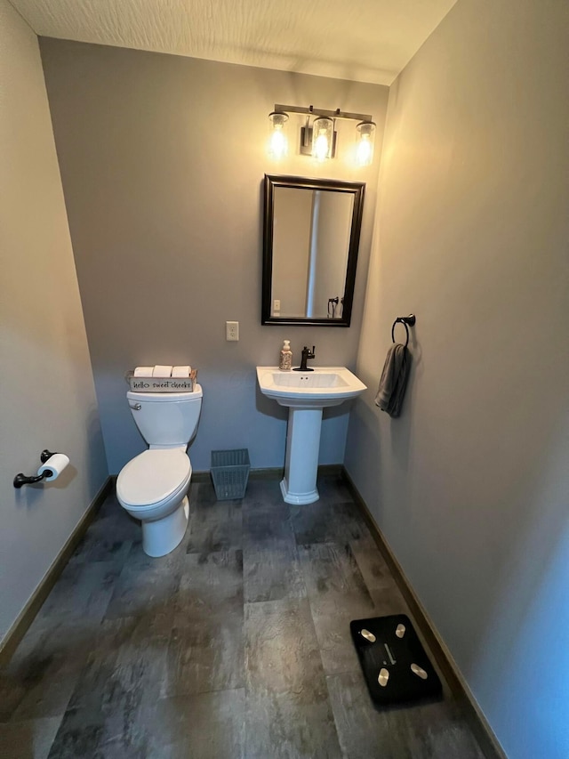 half bathroom featuring baseboards, toilet, and wood finished floors