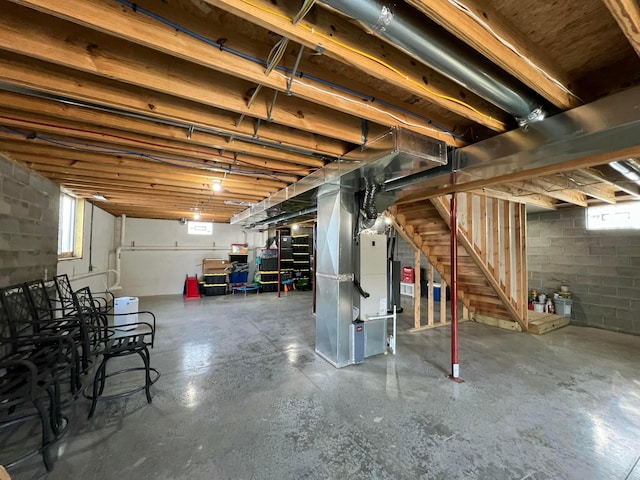 below grade area featuring heating unit, stairway, and concrete block wall