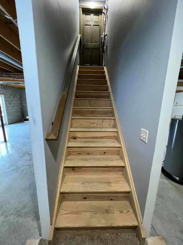 staircase featuring concrete flooring, water heater, and baseboards