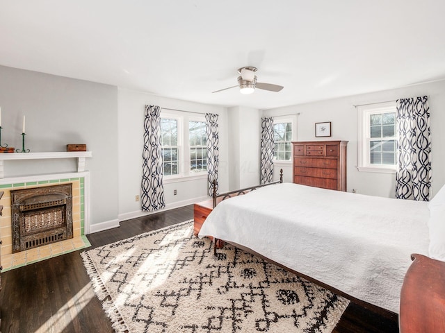 bedroom featuring dark hardwood / wood-style flooring, a tiled fireplace, and ceiling fan