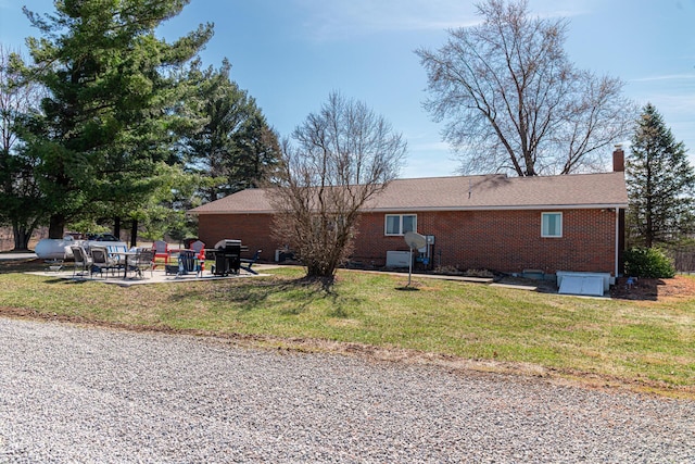 back of property featuring brick siding, a yard, a chimney, and a patio