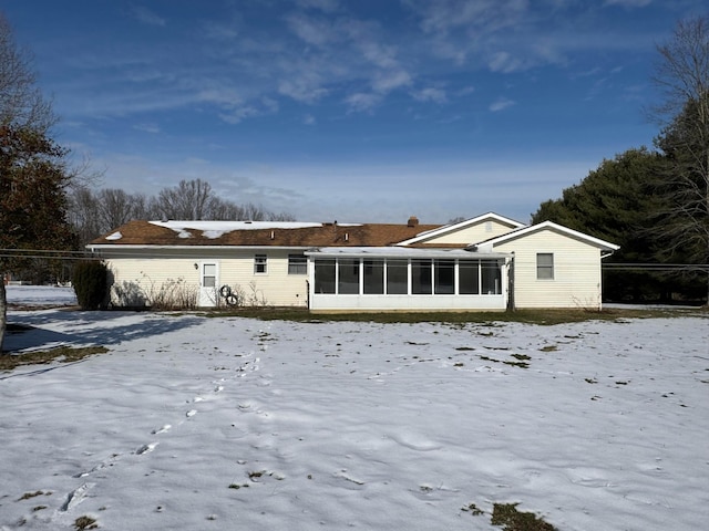 snow covered rear of property with a sunroom