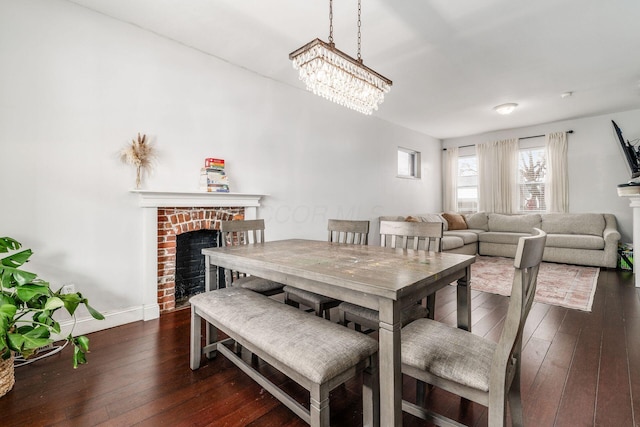 dining room with dark wood-type flooring, an inviting chandelier, and a fireplace