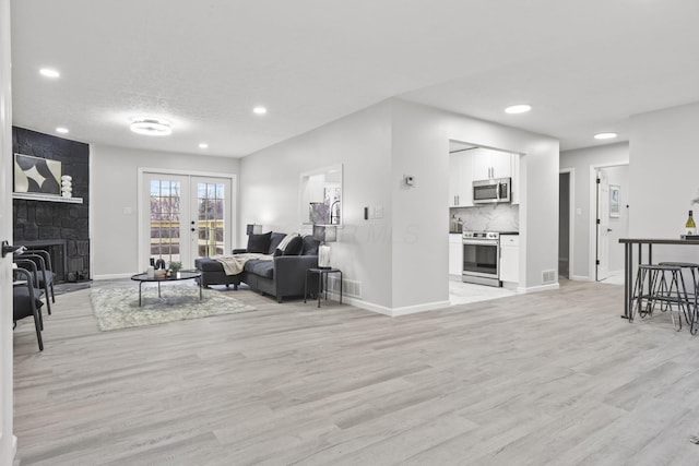 living room with french doors, a large fireplace, light hardwood / wood-style floors, and a textured ceiling