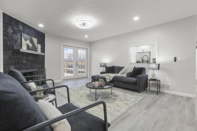 living room featuring french doors, a fireplace, light hardwood / wood-style floors, and a textured ceiling