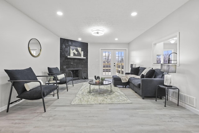 living room featuring a large fireplace, light hardwood / wood-style floors, french doors, and a textured ceiling