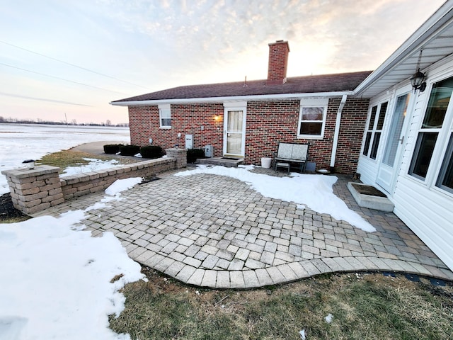 snow covered back of property featuring a patio