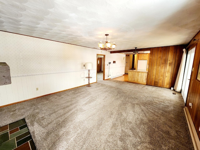 unfurnished living room featuring crown molding, an inviting chandelier, wooden walls, carpet, and a textured ceiling