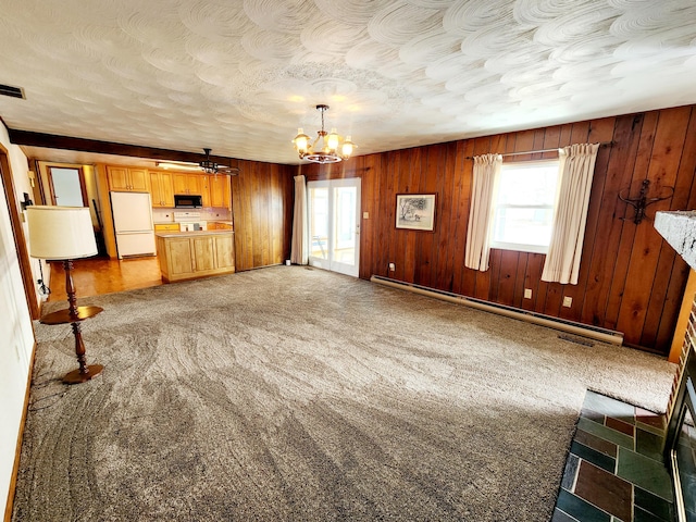 unfurnished living room with carpet floors, a baseboard heating unit, a chandelier, and wood walls