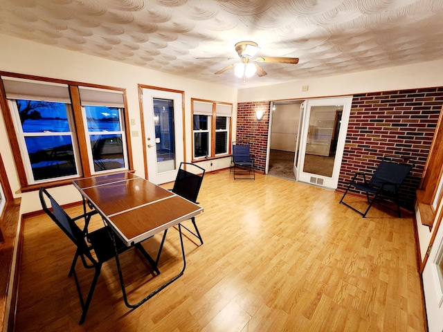 dining area with ceiling fan, brick wall, and light wood-type flooring