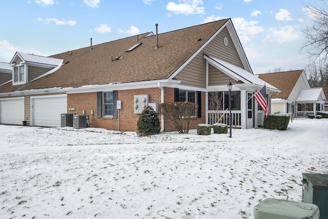 snow covered property featuring central AC and a garage