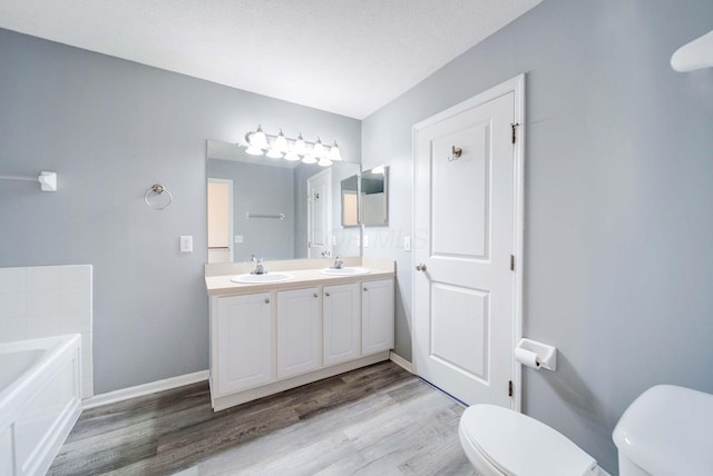 bathroom featuring toilet, a textured ceiling, vanity, a bath, and hardwood / wood-style flooring