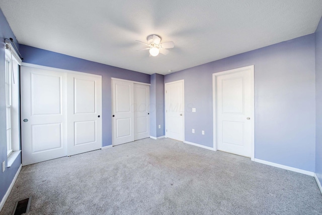 unfurnished bedroom with carpet, two closets, and ceiling fan