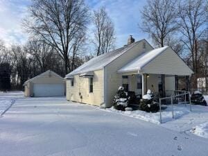 view of snowy exterior featuring a garage, an outdoor structure, and a porch