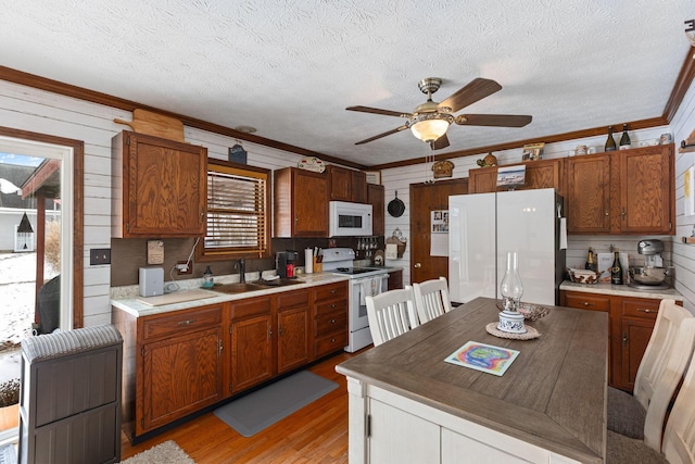 kitchen with crown molding, a textured ceiling, white appliances, and light hardwood / wood-style flooring