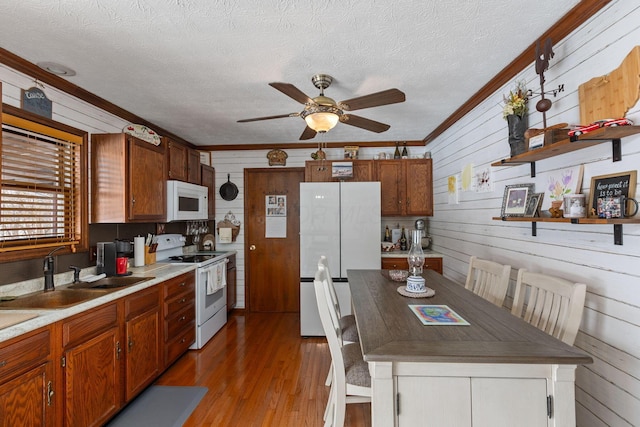 kitchen featuring sink, crown molding, white appliances, wooden walls, and a textured ceiling