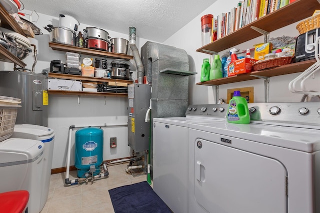 washroom with light tile patterned floors, washing machine and dryer, water heater, and a textured ceiling