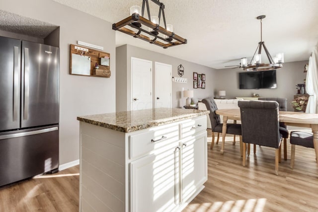 kitchen featuring stainless steel fridge, dark stone countertops, a textured ceiling, white cabinets, and decorative light fixtures