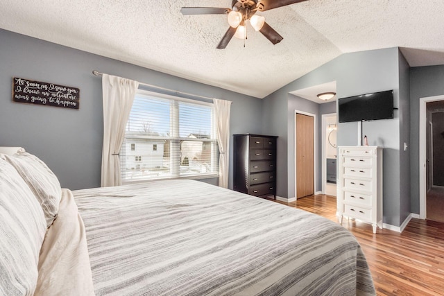 bedroom with a textured ceiling, vaulted ceiling, ceiling fan, and light wood-type flooring