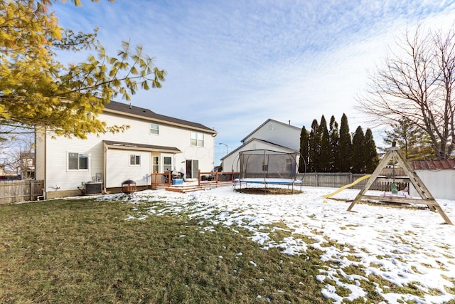 snowy yard featuring a wooden deck, a playground, a trampoline, and central air condition unit