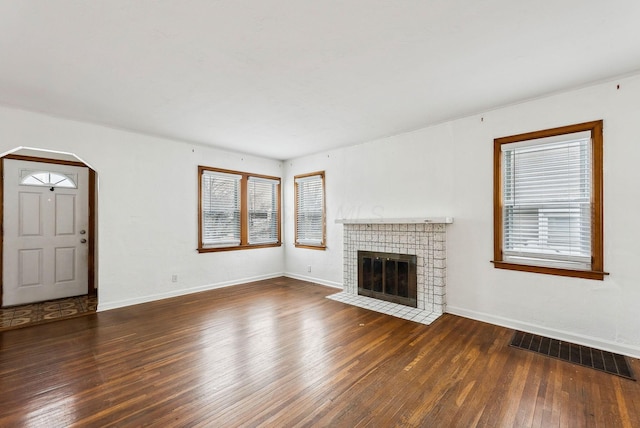 unfurnished living room featuring dark wood-type flooring and a tiled fireplace