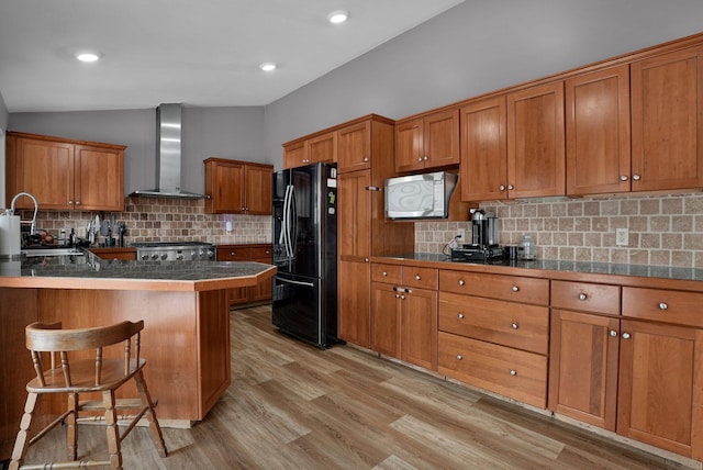 kitchen with wall chimney range hood, black refrigerator, stove, a kitchen breakfast bar, and kitchen peninsula