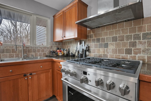 kitchen featuring high end stove, a sink, wall chimney range hood, brown cabinetry, and dark countertops