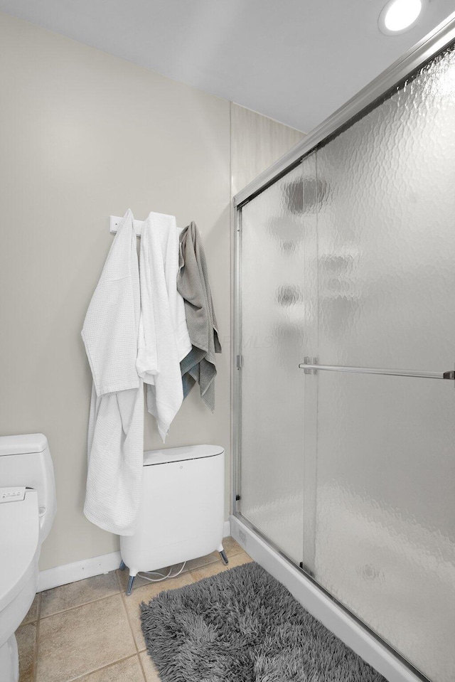 bathroom featuring toilet, a shower with shower door, and tile patterned flooring